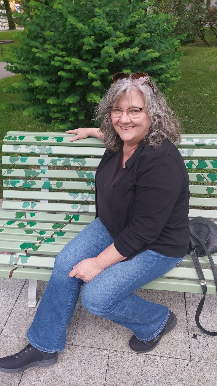 Portrait: lächelnd auf einer bemalten Parkbank vor grünen Sträuchern