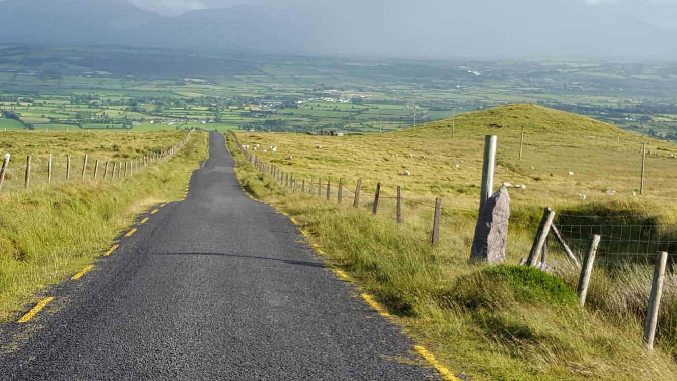 Schmale Straße, die über weite grüne Hügel zum Horizont führt